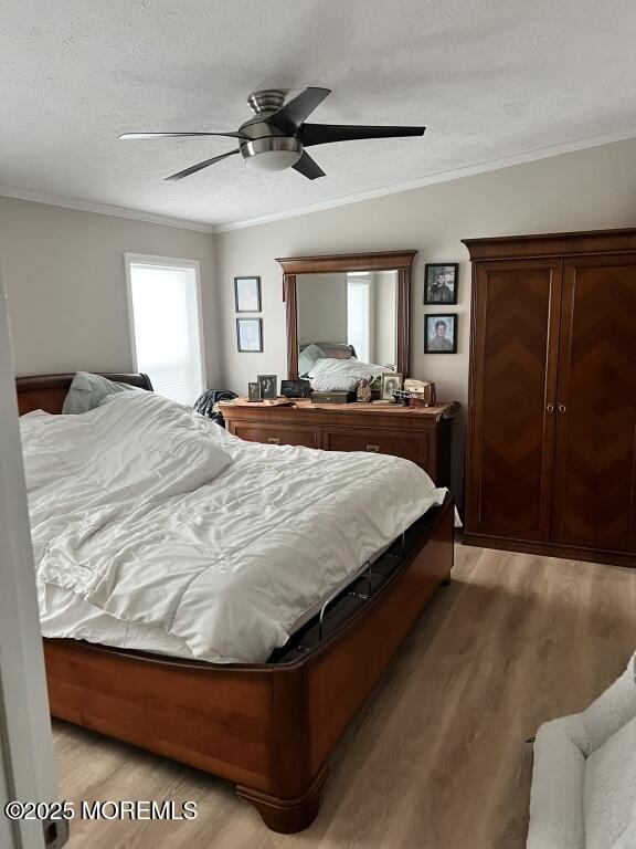 bedroom with a textured ceiling, ceiling fan, ornamental molding, and wood finished floors