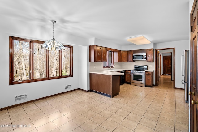 kitchen with a peninsula, a sink, baseboards, light countertops, and appliances with stainless steel finishes