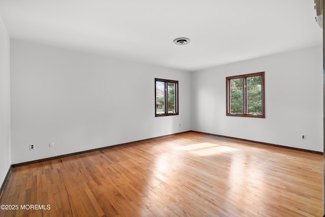 empty room with light wood finished floors, baseboards, and visible vents