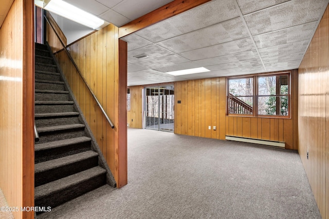 below grade area featuring carpet floors, wood walls, a healthy amount of sunlight, and baseboard heating