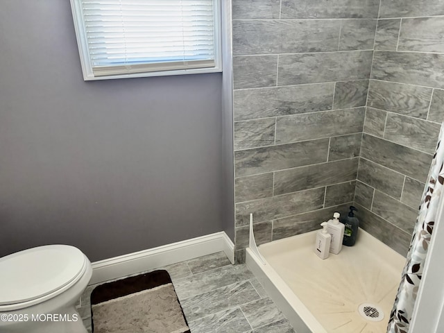 bathroom with toilet, a shower stall, and baseboards