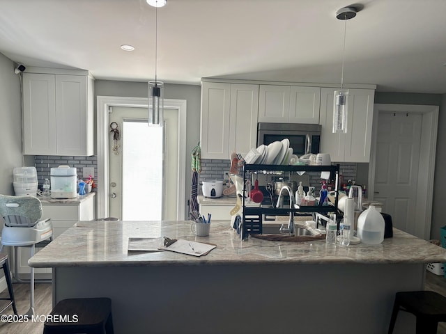 kitchen featuring stainless steel microwave, backsplash, white cabinets, and pendant lighting