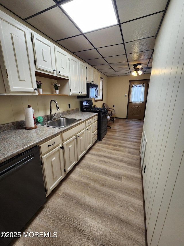 kitchen featuring light countertops, light wood-type flooring, black appliances, open shelves, and a sink