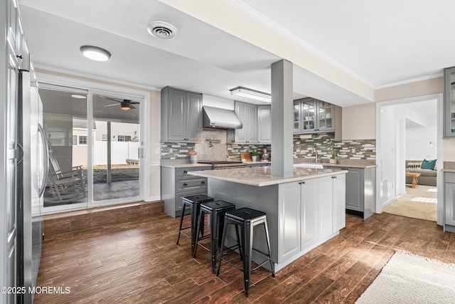 kitchen featuring visible vents, gray cabinetry, appliances with stainless steel finishes, wall chimney exhaust hood, and crown molding