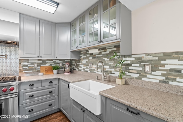 kitchen with decorative backsplash, gray cabinets, a sink, glass insert cabinets, and high end range