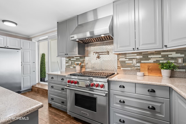 kitchen featuring gray cabinetry, ornamental molding, decorative backsplash, appliances with stainless steel finishes, and wall chimney exhaust hood