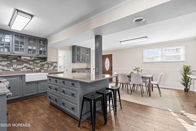 kitchen featuring a sink, a kitchen island, gray cabinets, a kitchen breakfast bar, and dark wood-style flooring