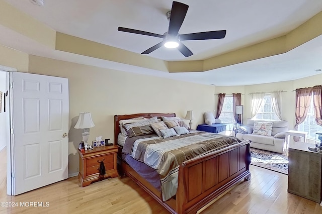 bedroom with light wood-style floors, ceiling fan, and a tray ceiling