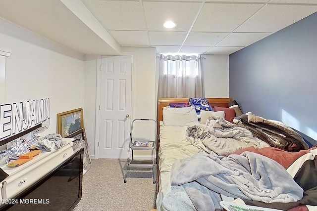 bedroom with a drop ceiling and light colored carpet