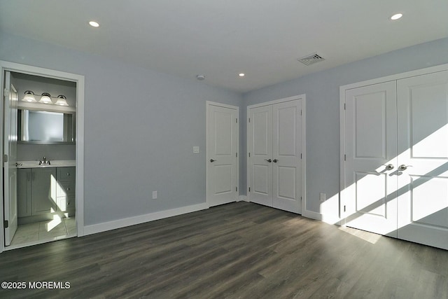 unfurnished bedroom featuring multiple closets, dark wood finished floors, visible vents, and a sink