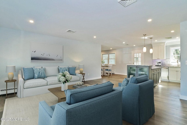 living room featuring baseboards, visible vents, wood finished floors, and recessed lighting