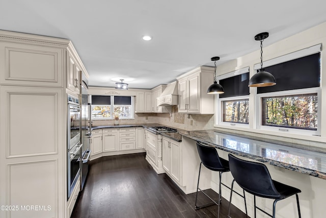 kitchen with a breakfast bar area, premium range hood, hanging light fixtures, and dark stone countertops