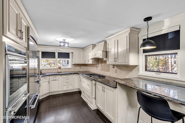 kitchen with stainless steel appliances, dark wood-style flooring, hanging light fixtures, custom exhaust hood, and dark stone counters