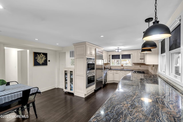 kitchen with dark stone counters, appliances with stainless steel finishes, decorative backsplash, dark wood-style floors, and pendant lighting