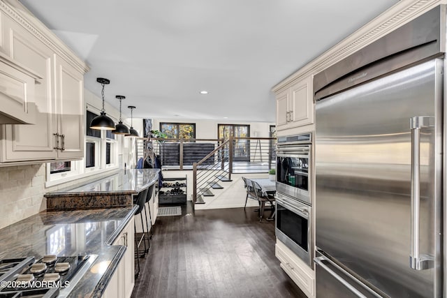 kitchen featuring pendant lighting, dark wood finished floors, decorative backsplash, appliances with stainless steel finishes, and dark stone countertops