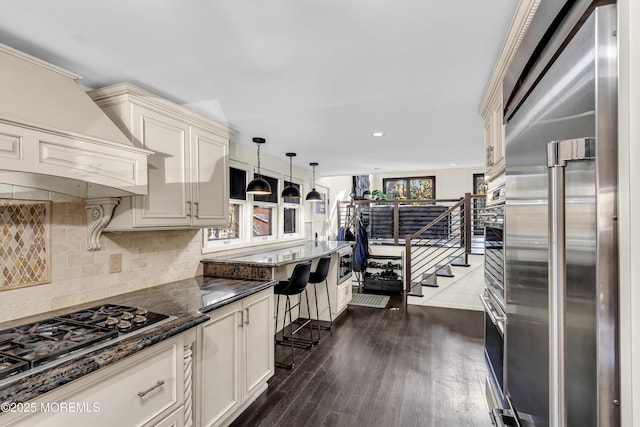 kitchen featuring decorative light fixtures, dark wood finished floors, stainless steel appliances, backsplash, and premium range hood