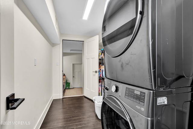clothes washing area with dark wood-style flooring, baseboards, stacked washing maching and dryer, and laundry area