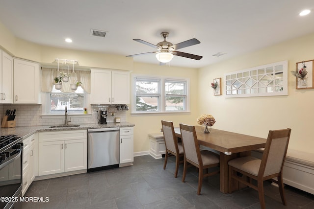 kitchen with light stone counters, stainless steel appliances, a sink, white cabinets, and backsplash