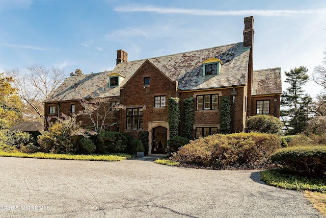 english style home featuring brick siding, a chimney, and a high end roof