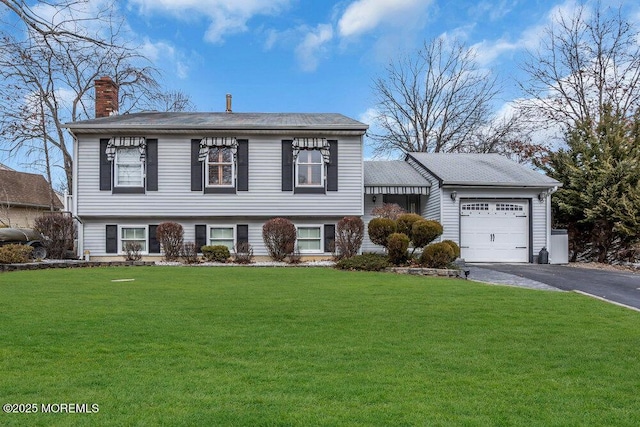 tri-level home with aphalt driveway, a chimney, an attached garage, and a front yard