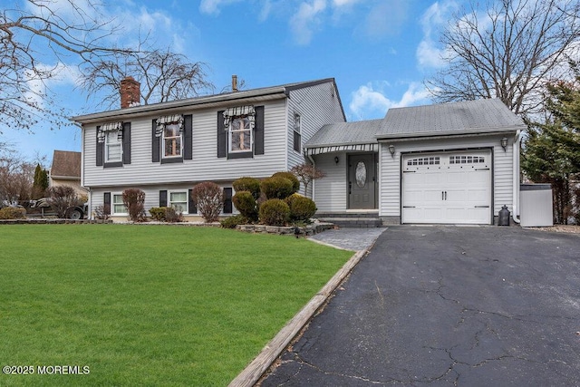 split level home with aphalt driveway, a chimney, an attached garage, and a front yard