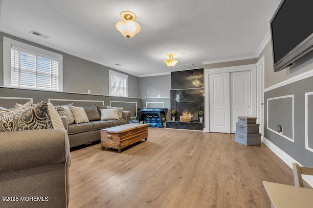 living room with wood finished floors, visible vents, baseboards, a tiled fireplace, and crown molding