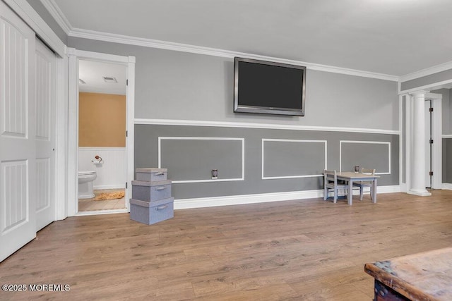 interior space featuring ornate columns, crown molding, wood finished floors, and a wainscoted wall