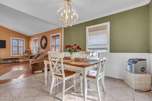 dining room with a wainscoted wall, crown molding, light tile patterned floors, lofted ceiling, and a chandelier