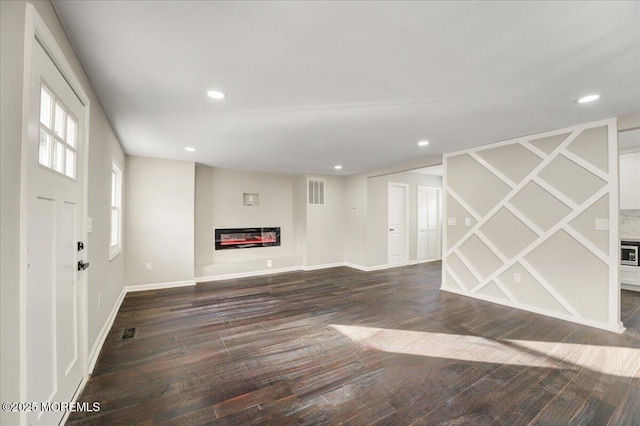 unfurnished living room featuring recessed lighting, visible vents, dark wood-type flooring, and a glass covered fireplace