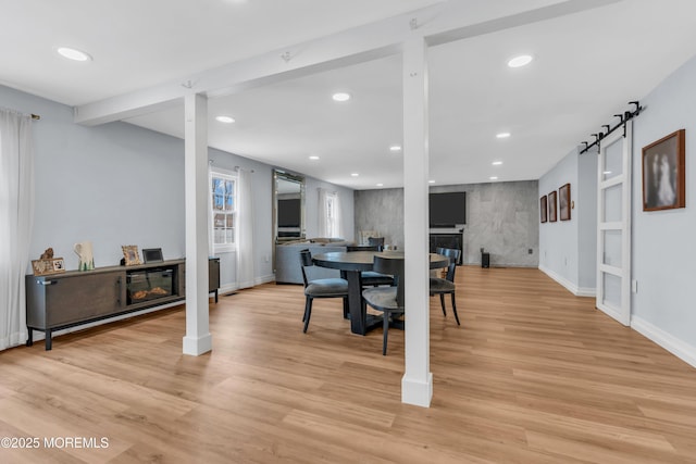 dining space featuring a barn door, a fireplace, light wood-style flooring, and recessed lighting