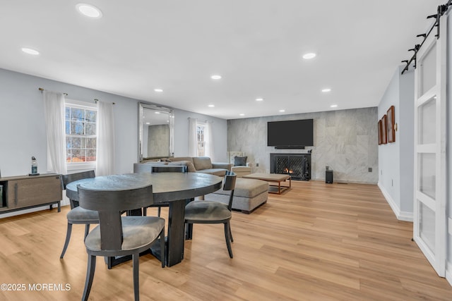 dining space with an accent wall, a barn door, recessed lighting, and light wood-style floors