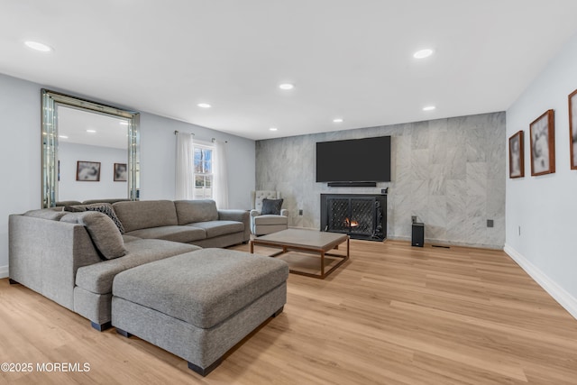 living area with light wood finished floors, recessed lighting, an accent wall, a warm lit fireplace, and baseboards