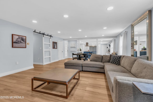 living room featuring recessed lighting, baseboards, light wood finished floors, and a barn door