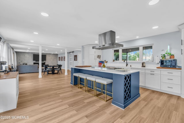 kitchen featuring light wood finished floors, a center island, island exhaust hood, light countertops, and white cabinetry