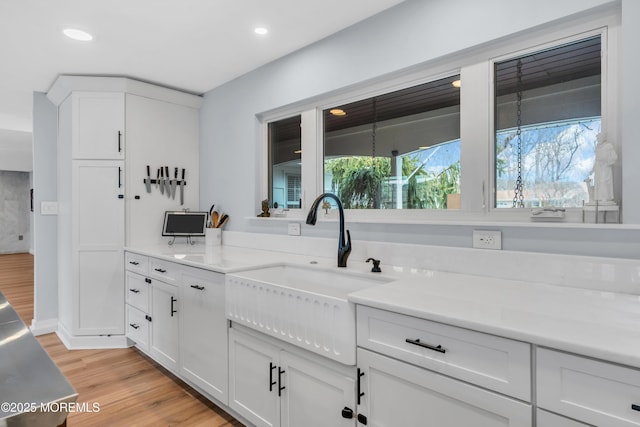 kitchen with white cabinets, light countertops, light wood-style floors, a sink, and recessed lighting