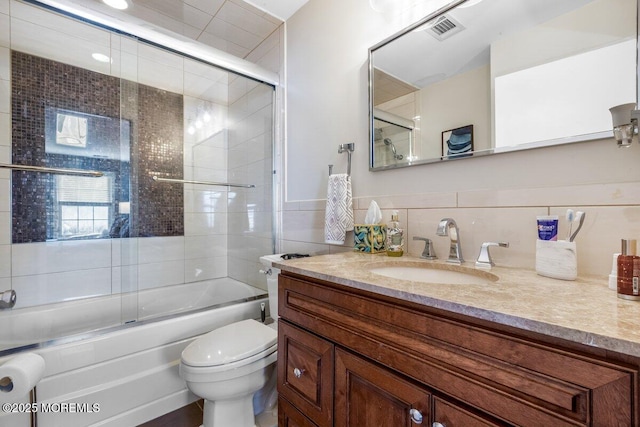 full bath featuring tile walls, visible vents, toilet, combined bath / shower with glass door, and vanity