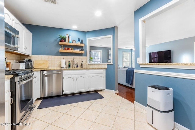 kitchen featuring light tile patterned floors, backsplash, appliances with stainless steel finishes, white cabinetry, and a sink