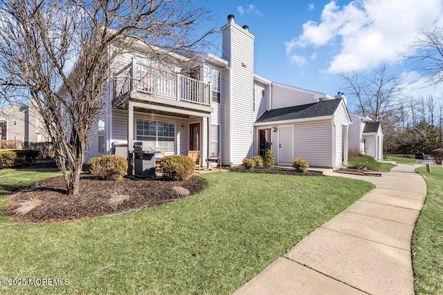 view of front of house with a front yard, a chimney, and a balcony