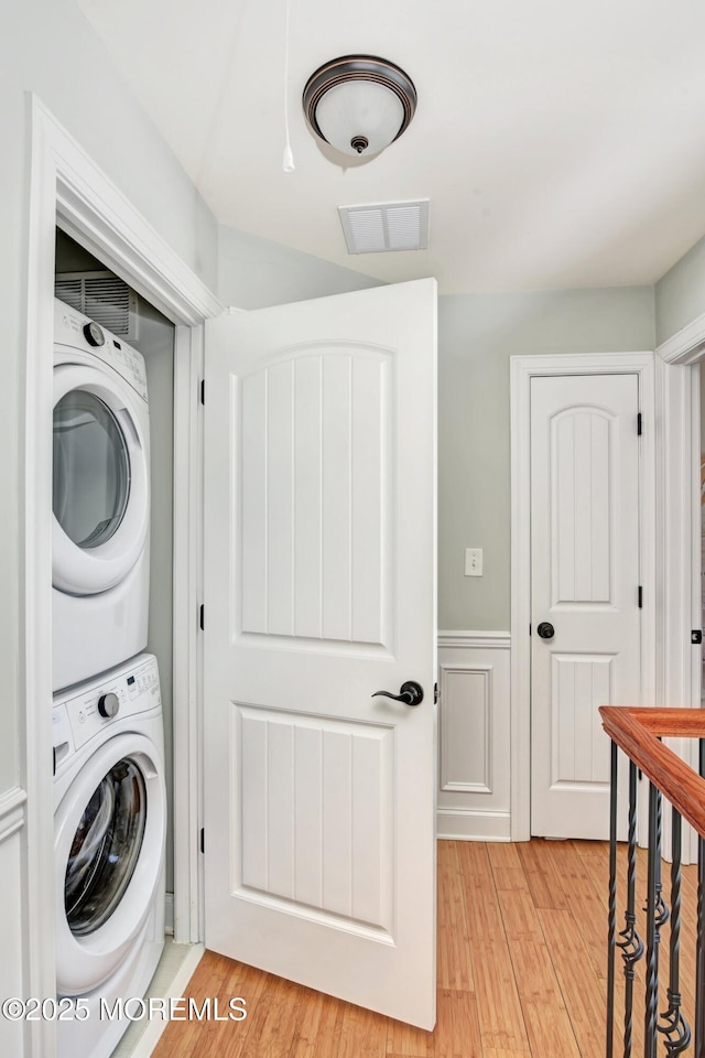 clothes washing area featuring a wainscoted wall, laundry area, stacked washer / dryer, visible vents, and light wood-style floors