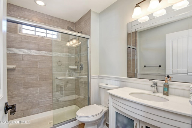 full bath with a stall shower, wainscoting, vanity, and toilet