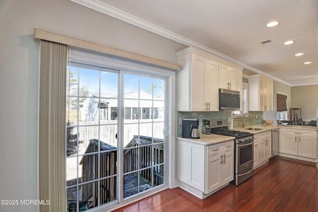 kitchen with dark wood finished floors, ornamental molding, a sink, stainless steel appliances, and backsplash