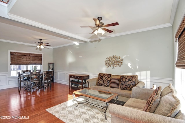 living area featuring ceiling fan, a decorative wall, wood finished floors, ornamental molding, and wainscoting