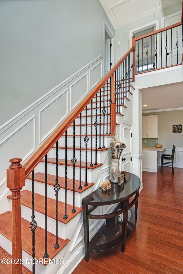 staircase featuring attic access, ornamental molding, a decorative wall, and wood finished floors