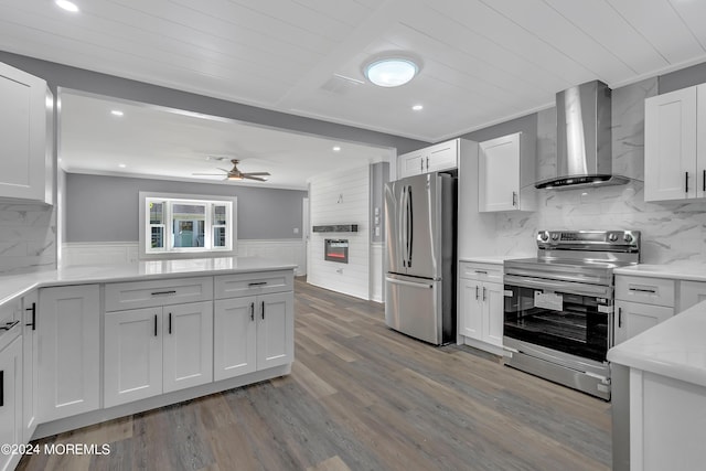 kitchen featuring wood finished floors, stainless steel appliances, crown molding, wall chimney range hood, and white cabinetry