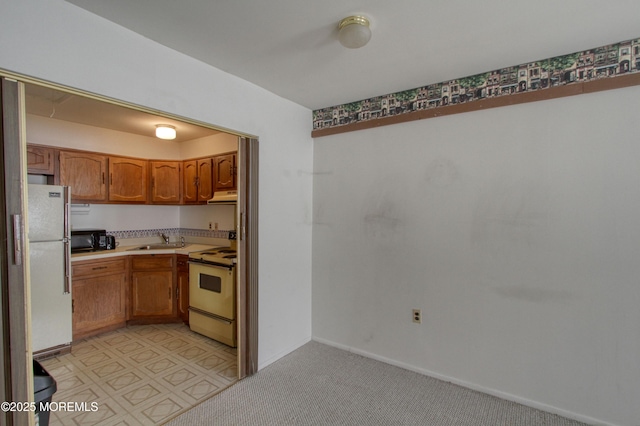 kitchen with under cabinet range hood, white appliances, a sink, light countertops, and brown cabinetry