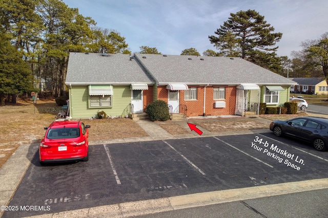 view of front facade with uncovered parking, brick siding, and roof with shingles