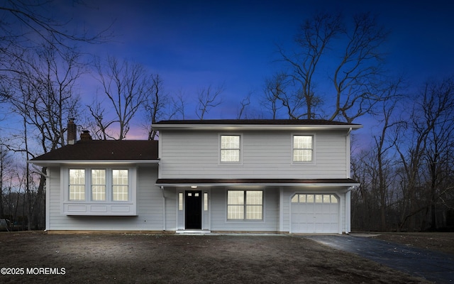 view of front of house featuring an attached garage, a chimney, and aphalt driveway