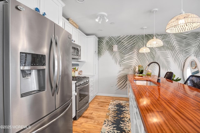 kitchen with a sink, white cabinets, wooden counters, appliances with stainless steel finishes, and wallpapered walls