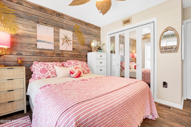 bedroom featuring ceiling fan, wood walls, wood finished floors, visible vents, and baseboards