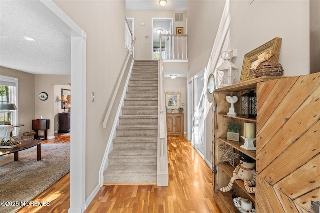 stairway with a textured ceiling, wood finished floors, visible vents, and baseboards